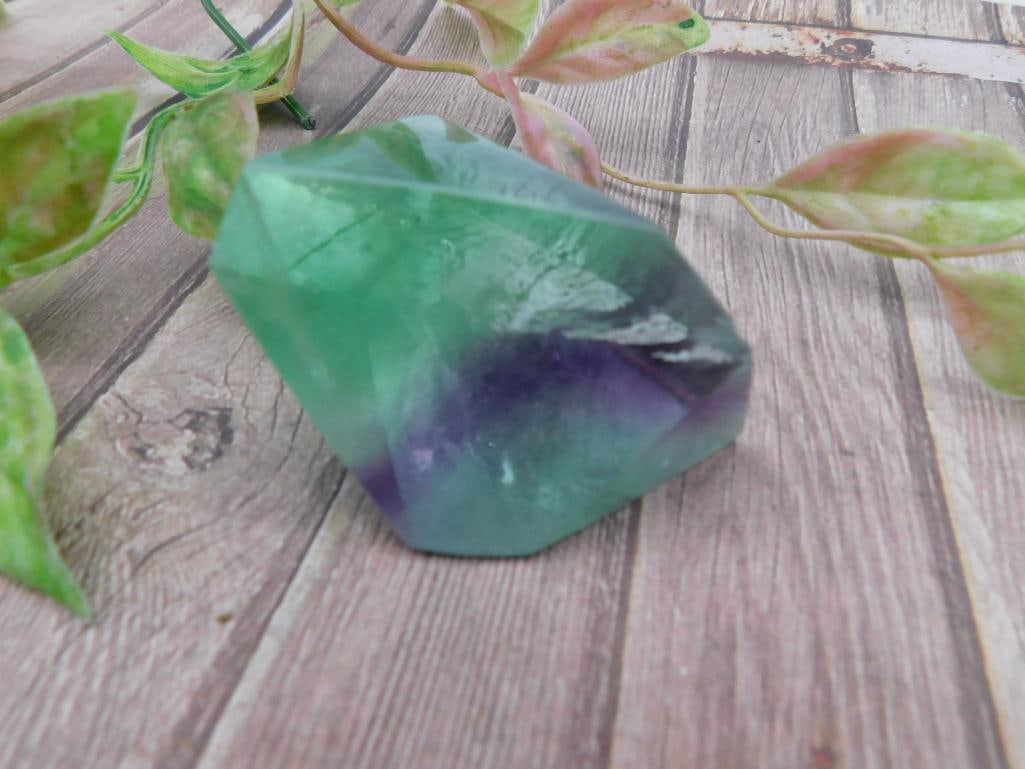 Green and Purple Fluorite Gemstone Specimen: Green and purple fluorite gemstone specimen featuring semi-polished surfaces. Approximately 103 grams in weight. Displayed on a wooden surface with a ruler for scale. Ideal for collectors or as a deco