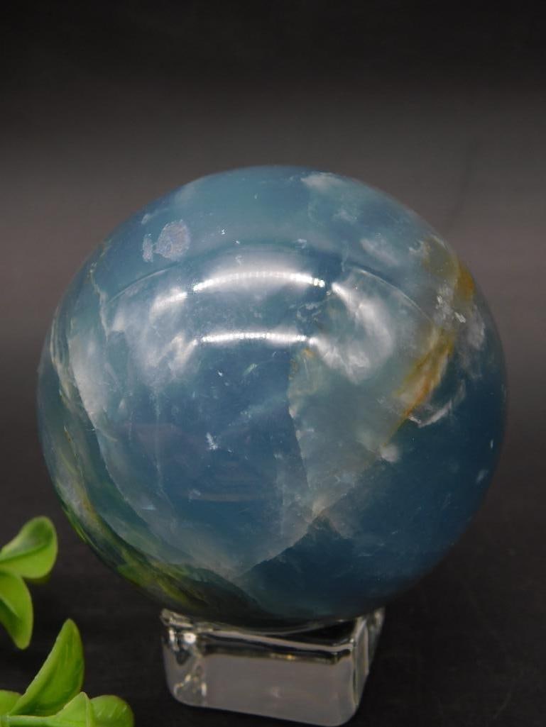 Polished Blue Agate Sphere: Polished blue agate sphere featuring natural banding and variations in color. Includes a clear acrylic stand for display. Weighs approximately 337 grams. Ideal as a collectible or display piece.