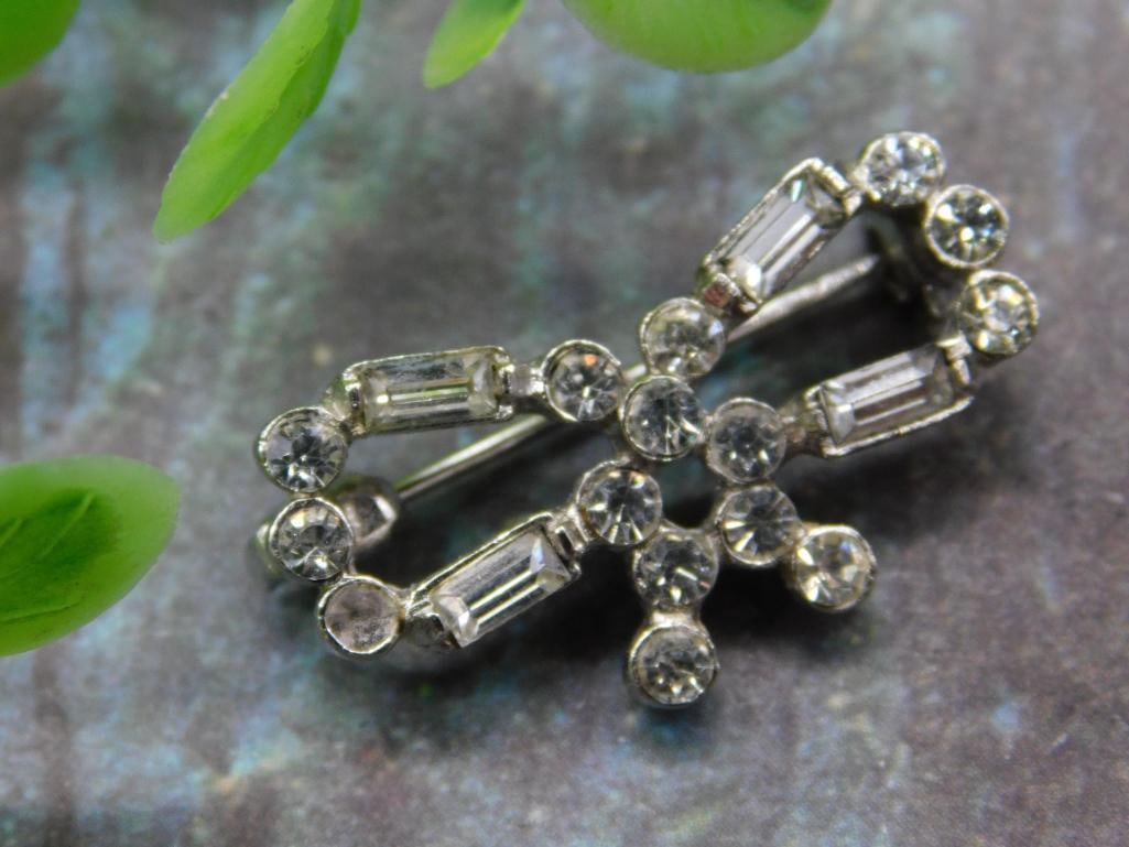 Crystal Bow Shaped Brooch Pin with Stone Accents: Bow-shaped brooch featuring multiple clear crystal stones of varying sizes, including round and rectangular cuts. Silver-tone metal structure with a secure pin-back clasp. Compact design ideal for dec