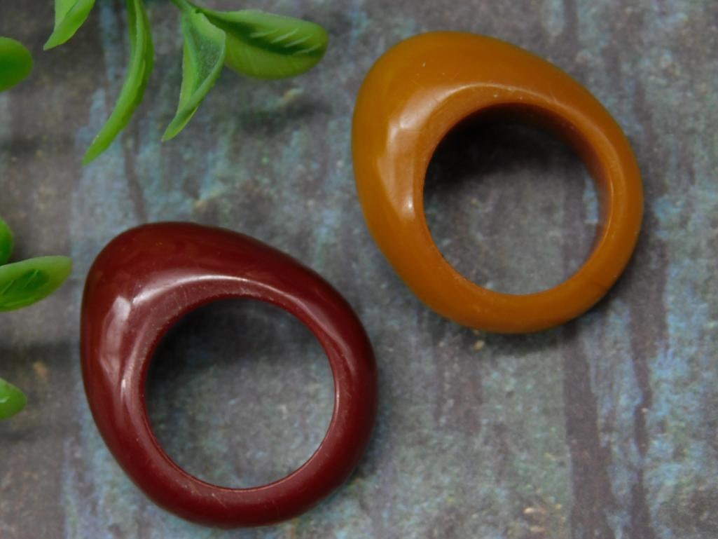 Pair of Bakelite Saddle Rings in Earth Tones: Pair of Bakelite saddle-shaped rings in rich earth tones, one in maroon and the other in caramel. Unique, slightly irregular shapes. Lightweight and collectible pieces. Suitable for display or wear. U
