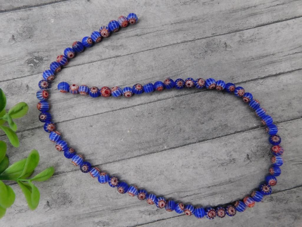 AFRICAN TRADE BEADS: This is a strand of millefiori glass beads featuring blue and red designs with floral-like patterns. The strand consists of evenly sized beads, with a total length depicted in the image. It is ideal f