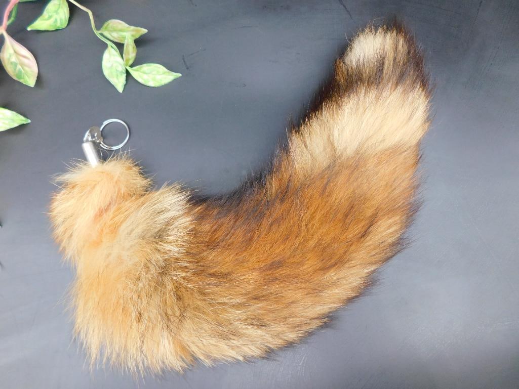 RED FOX Fur Keychain Tail With Metal Ring Attachment: Real fur tail keychain with metal ring attachment. The tail is predominantly brown with shades of darker and lighter tones. Attached metal ring allows for easy fastening to keys or bags. Features a fl