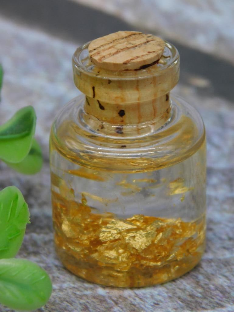 Mini Glass Bottle With 22K Gold Flakes: Miniature glass bottle containing real 22K gold flakes. The bottle is sealed with a cork stopper and presented as part of a collectible auction lot. Includes a label indicating 'Real 22K Gold Flakes' 