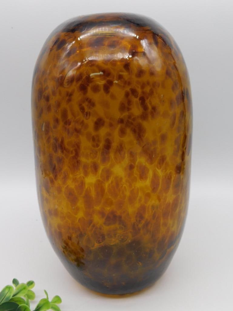 Amber Speckled Glass Vase With Rounded Shape: Amber glass vase featuring a speckled amber and brown pattern. Rounded, bulbous form with a small opening at the top. Smooth finish with a polished surface. Appears to be hand-blown or handcrafted. Si
