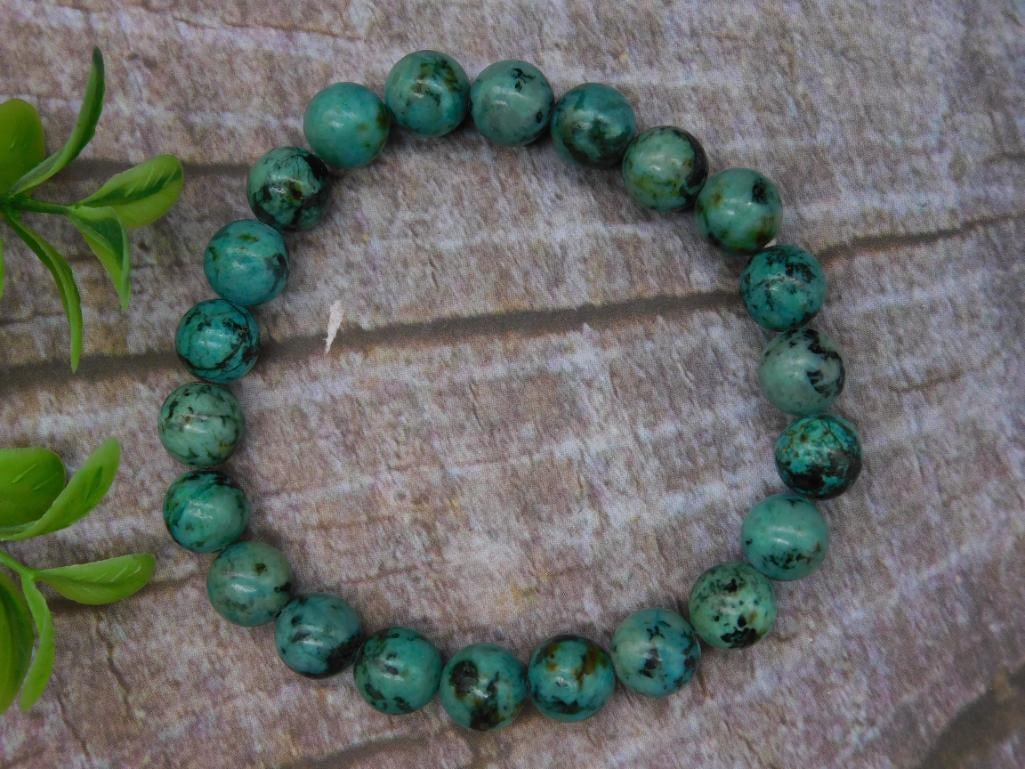 Green and Black Beaded Bracelet with Round Stones: This bracelet features round green stones with black inclusions. It contains approximately 20 beads of uniform size, strung together on elastic. The coin pictured provides a visual scale. Perfect for 
