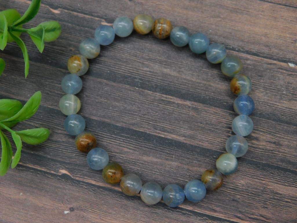 Beaded Blue and Brown Stone Bracelet: A stretchable beaded bracelet featuring polished blue and brown stone beads. Each bead is rounded and uniformly shaped, contributing to a consistent design. The bracelet is displayed next to a U.S. qu