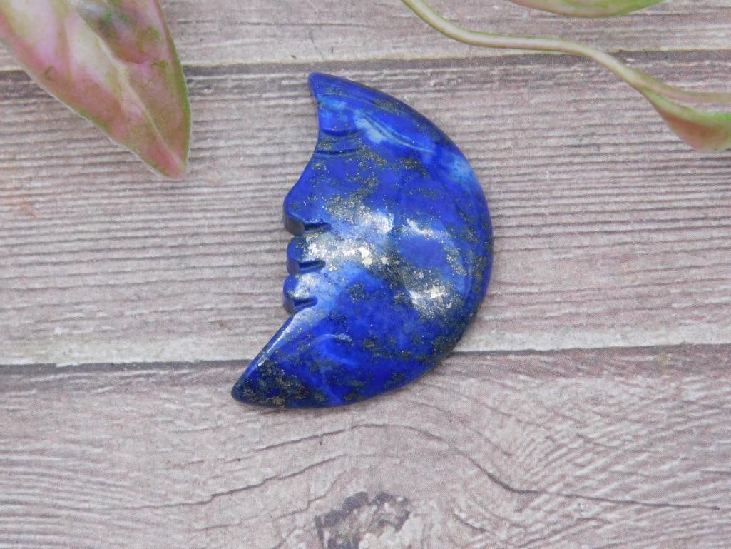 Lapis Lazuli Crescent Moon Carved Stone: Lapis lazuli crescent moon carving with deep blue tones and gold flecks. The piece features a face profile. Included for scale is a ruler indicating a size slightly under 2 inches. Ideal for collectio