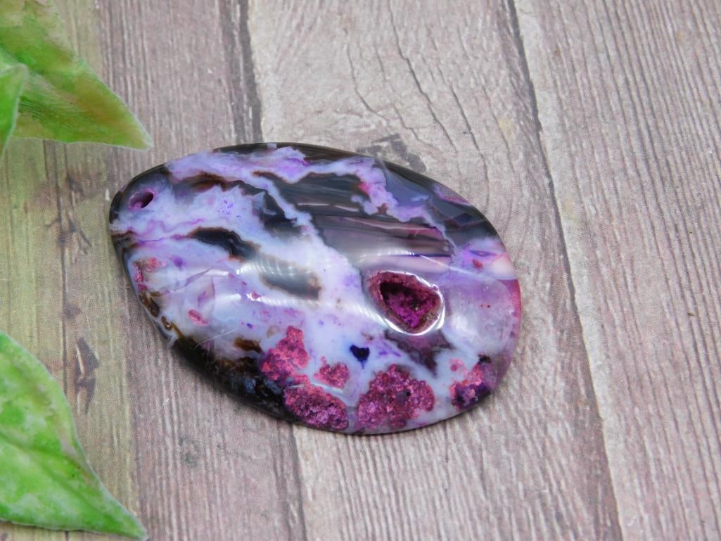 Purple and Pink Stone Pendant with Natural Hole: Purple and pink polished stone pendant featuring natural patterns and a hole for hanging. Measures approximately 2 inches in length judging by the scale provided. Ideal for jewelry making or as a disp