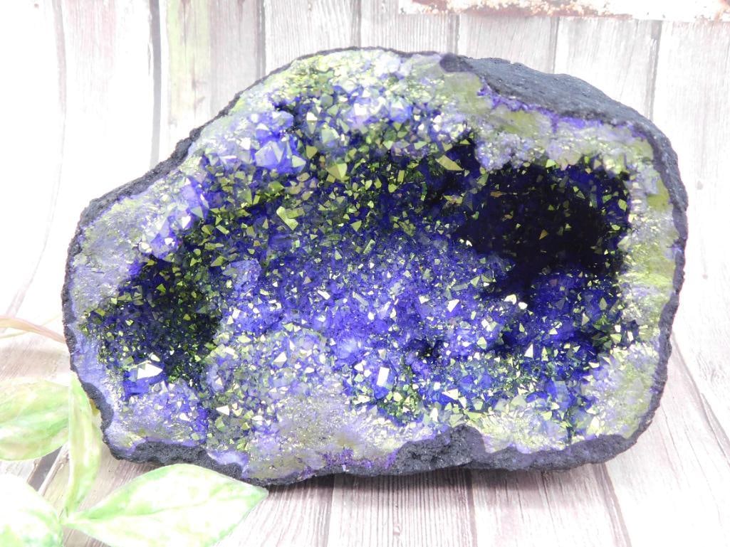 Large Geode Cluster with Purple and Green Crystals: This is a large geode featuring vibrant purple and green crystals. The geode displays a rough outer surface and a sparkling crystal-filled cavity. It weighs 8 grams, as noted on the included label. Th