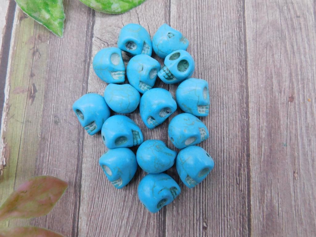 Lot of Small Blue Skull Shaped Beads: This group includes multiple small blue skull-shaped beads. Each bead appears to have detailing typical of a skull design. The beads are displayed with a ruler for size reference, though specific dime