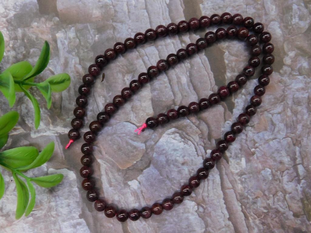 Strand of Dark Red Garnet Beads: This lot features a single strand of polished dark red garnet beads. The beads are uniformly spherical and strung on pink thread. The strand's total length is shown against a ruler, measuring approxim