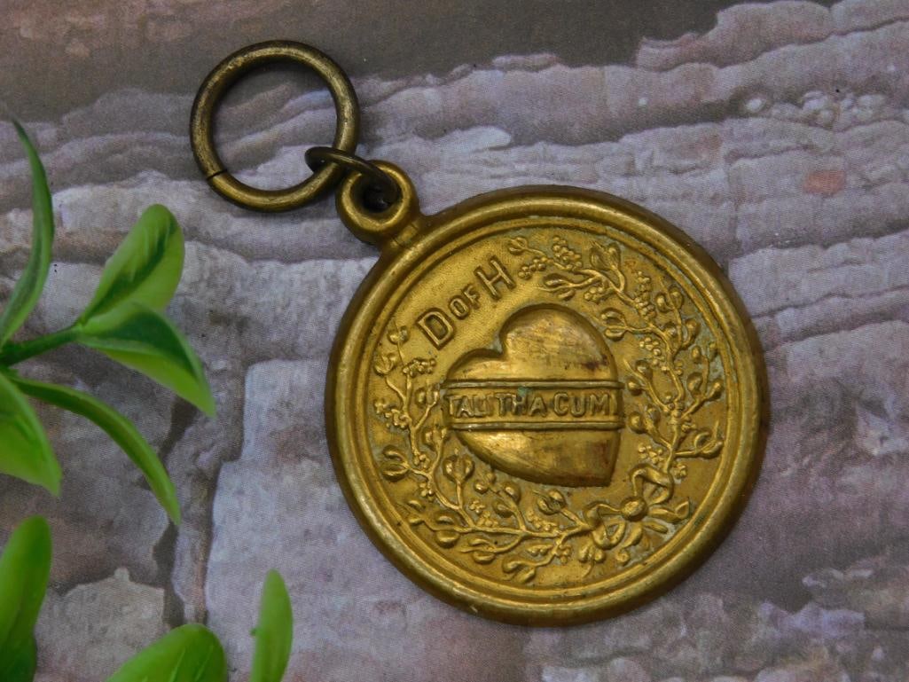 Gold-Colored Talithacumi Religious Pendant: Gold-colored round religious pendant featuring the inscription "Talithacumi" inside a heart design surrounded by intricate floral detailing. Marked with "Dr. H" on the upper left corner. The reverse s