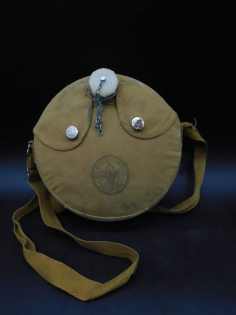 Boy Scouts of America Canvas Canteen with Strap: Boy Scouts of America canvas canteen featuring a stamped emblem on the front. Includes a shoulder strap for portability, a white plastic lid attached with a chain, and aluminum screw tops. The canteen