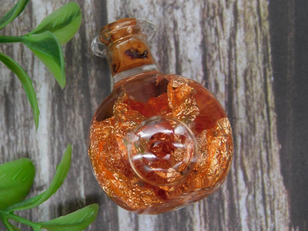 Small Glass Bottle With Metallic COPPER FLAKES: Small round glass bottle filled with metallic gold flakes. Features an ornamental stopper and a clear finish. Shown for scale next to a U.S. quarter. Appears to be intended as a decorative or collecti