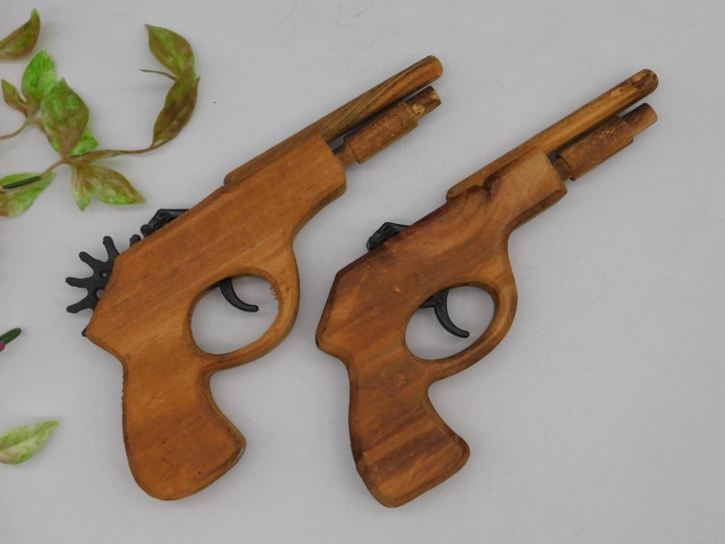 Pair of Wooden Rubber Band Guns with Plastic Mechanisms: This lot features a pair of wooden rubber band guns. Each gun is constructed from smooth-finished wood and includes plastic trigger and gear mechanisms for rubber band launching. Both guns exhibit a f
