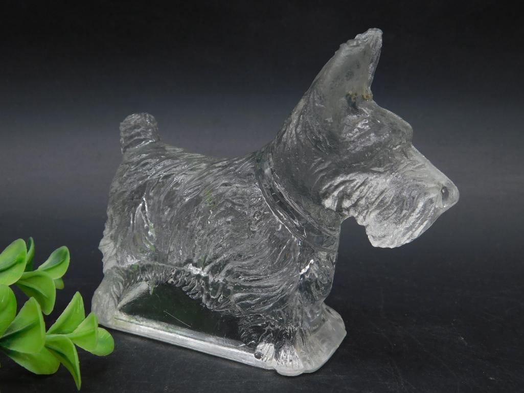 Clear Glass Dog Figurine in Scottie Dog Form: Clear glass figurine in the shape of a Scottie dog, featuring detailed fur texture and facial expression. Stands on a rectangular glass base. Suitable as a display item or collectible.