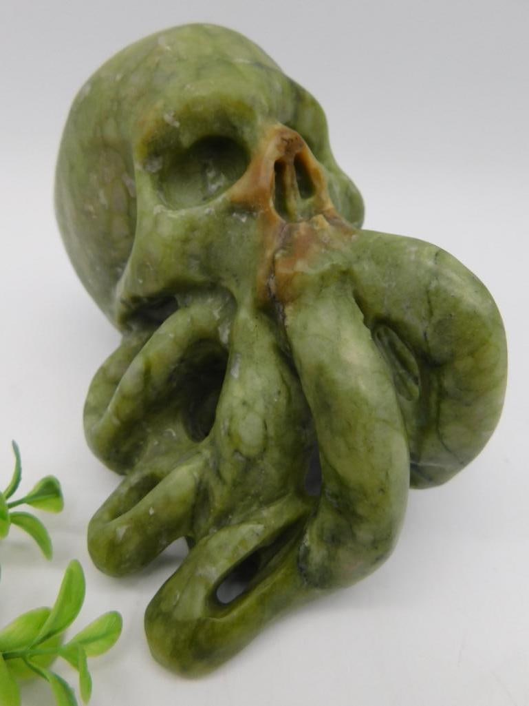 Green Jade Octopus and Skull Sculpture Rock Stone Lapidary Specimen: Green stone sculpture featuring a unique design combining an octopus with a skull motif. Intricately carved with detailed tentacles and hollow areas. Includes a blend of earthy tones with predominant