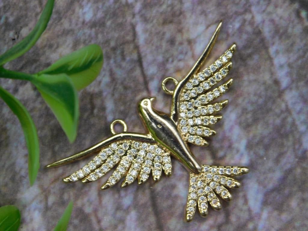 Gold-Plated Flying Bird Pendant with Pave Crystals: Gold-plated bird-shaped pendant with intricately designed wings. The wings and tail feature pave-set clear crystals. Includes two loops for attachment, ideal for integration into a necklace or bracele