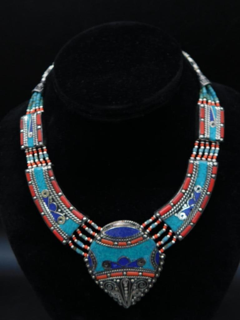 Turquoise, Lapis Lazuli, and Turquoise Beaded Necklace with Central Pendant: Striking necklace featuring intricate beadwork with turquoise, coral, and inlaid blue accents. The central pendant showcases detailed metal embellishments and vibrant colors. Designed with a blend of