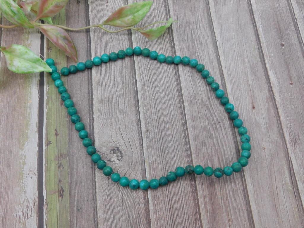 Green Round Beaded Necklace with Natural Stone Look: Green beaded necklace featuring round beads with a natural stone appearance. Beads are evenly sized and strung on a cord. The overall length of the necklace appears fixed, no clasp visible. Item inclu