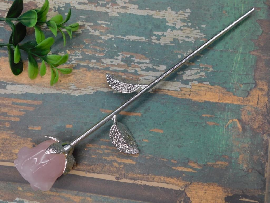 Carved Rose Quartz Flower on Metal Stem: This item features a carved rose quartz stone in the shape of a flower, mounted on a slender metal stem. The stem is adorned with textured metal leaves. The item showcases intricate carving details on