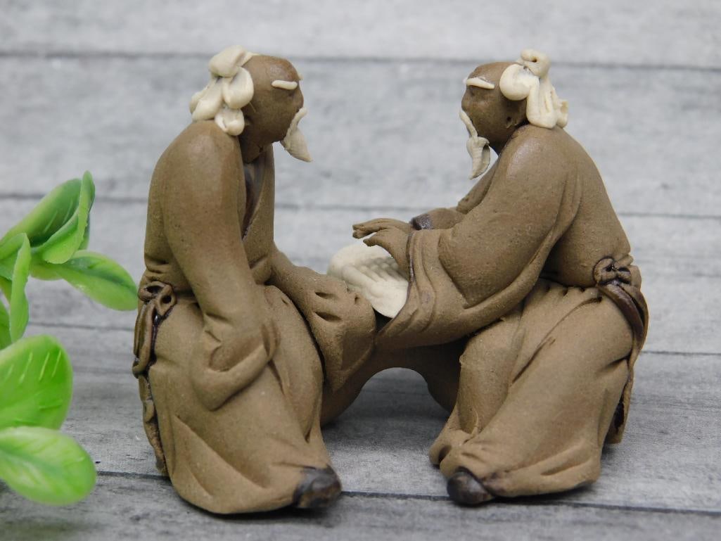 Ceramic Figurines of Two Seated Elderly Figures: Pair of finely detailed ceramic figurines depicting two seated elderly figures engaged in a conversation. The figures feature textured, natural-toned robes and carefully crafted facial details. Includ