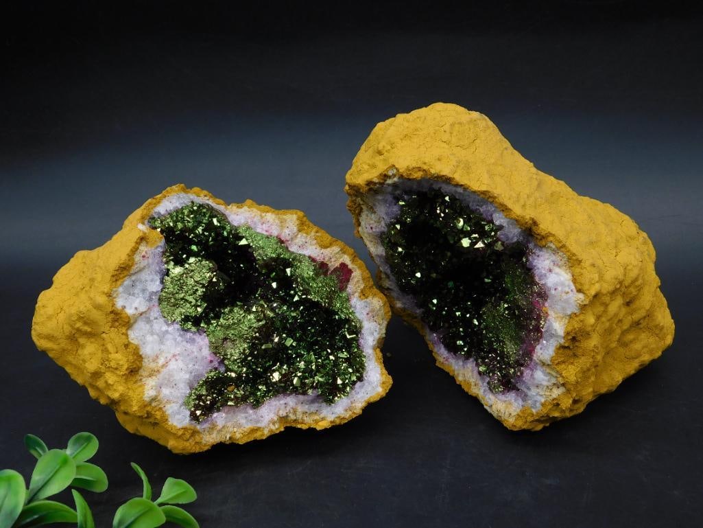 Geode Rock With Green Crystal Cluster: This geode features a golden outer shell with a vibrant green crystal cluster within. The crystal interior is highlighted against a background of white and purple hues. It is displayed halved, reveali