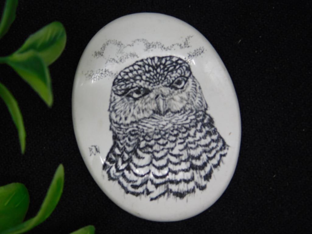 SCRIMSHAW CABOCHON With Owl Design: Oval-shaped ivory-colored stone featuring an etched owl design with intricate feather details. The etching depicts the owl?s head and upper body, surrounded by an abstract sketched background. Smooth