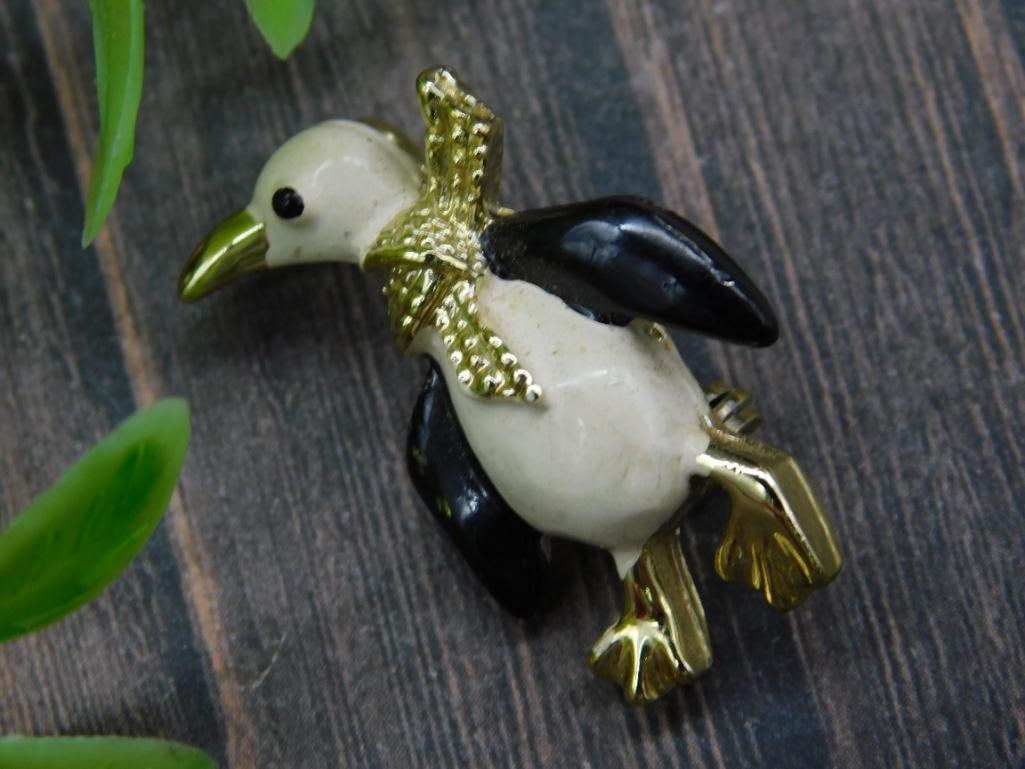 Gold-Toned Penguin Figurative Brooch with Black and White Accents: A gold-toned brooch shaped like a penguin, featuring black and white accents for detailing. Compact size as shown, with a quarter for scale comparison. Suitable for adding a statement to jackets, hats