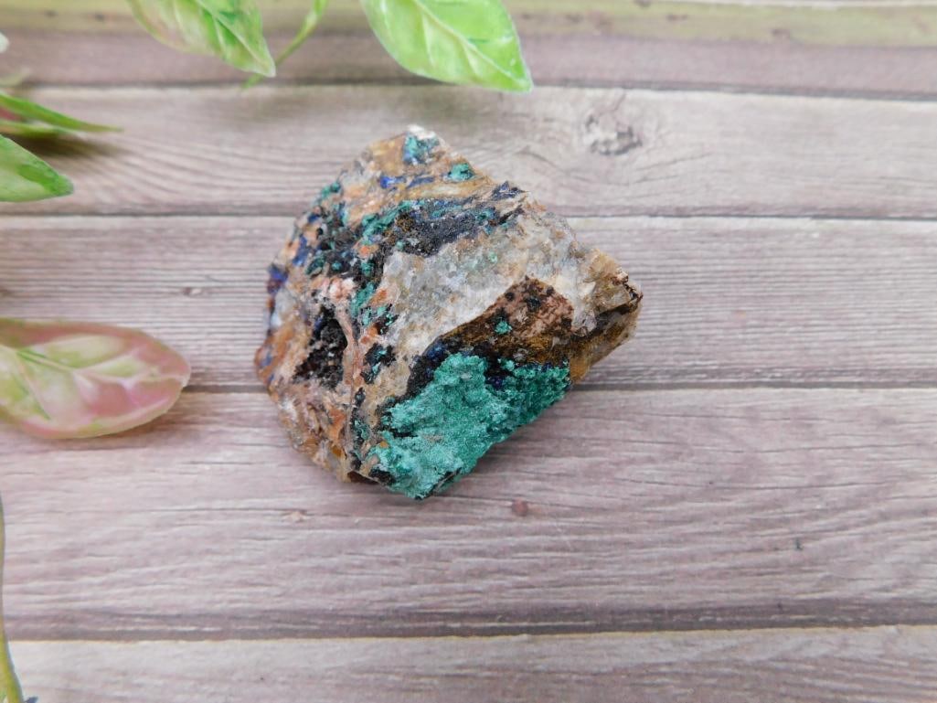Colorful Mineral Specimen With Green and Blue Hues: A visually striking mineral specimen featuring natural shades of vibrant green, blue, and earthy tones. The rock displays an intriguing combination of textures and colors, ideal for collectors. Includ