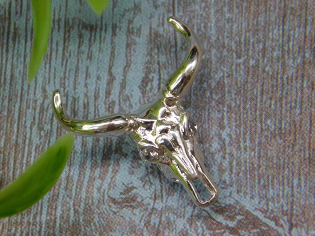 Metal Longhorn Skull Pendant with Polished Finish: Metal pendant in the shape of a longhorn skull with a polished finish. Features small size suitable for jewelry. Includes a loop for easy attachment to chains or cords.