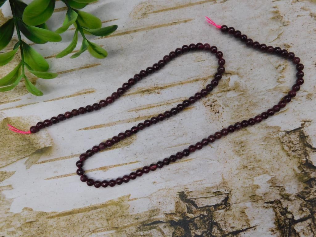Strand of Garnet Beads With Pink Thread: This listing features a strand of polished round garnet beads strung on pink thread. Each bead is uniform in size and exhibits a rich, deep hue. The strand measures approximately 16 inches in length. 