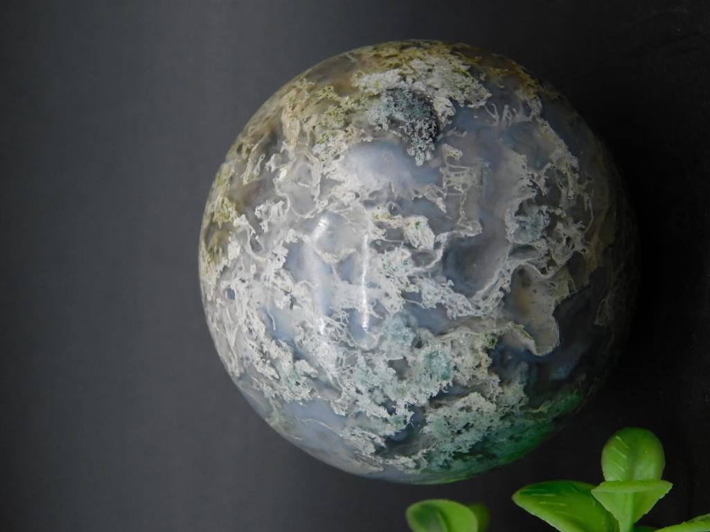 Moss Agate Sphere Weighing 174 Grams: Moss Agate sphere weighing 174 grams. Features intricate natural patterns and shades of gray, green, and white. Comes as a free-standing decorative piece. Ideal as a display item. Includes ruler in th