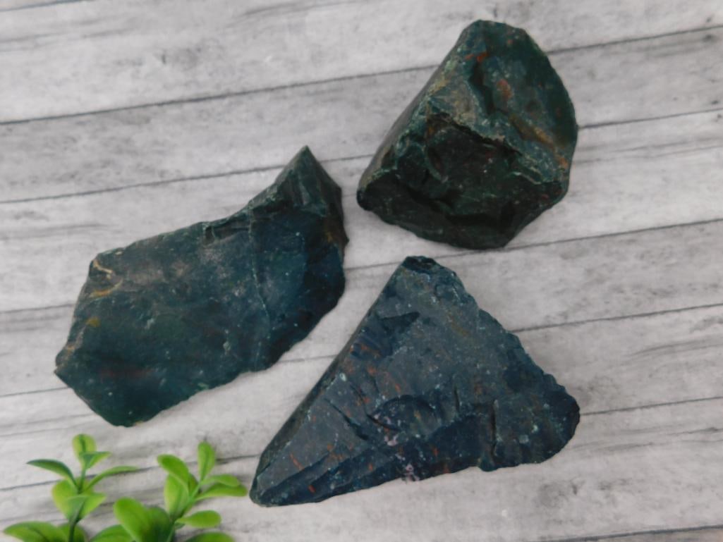 Set of Three Rough Bloodstone Specimens: Lot includes three rough bloodstone specimens. Exhibits characteristic deep green coloration with red spotting. Natural, unpolished stones as shown. Combined weight of approximately 265 grams.