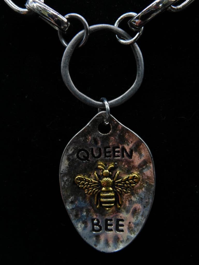 Chain Necklace with Queen Bee Charm: Silver-tone chain necklace featuring a hammered, teardrop-shaped charm with a bee design and 'Queen Bee' text. Chain is composed of oval links. Bee graphic and text are in gold-tone. Lobster clasp clo
