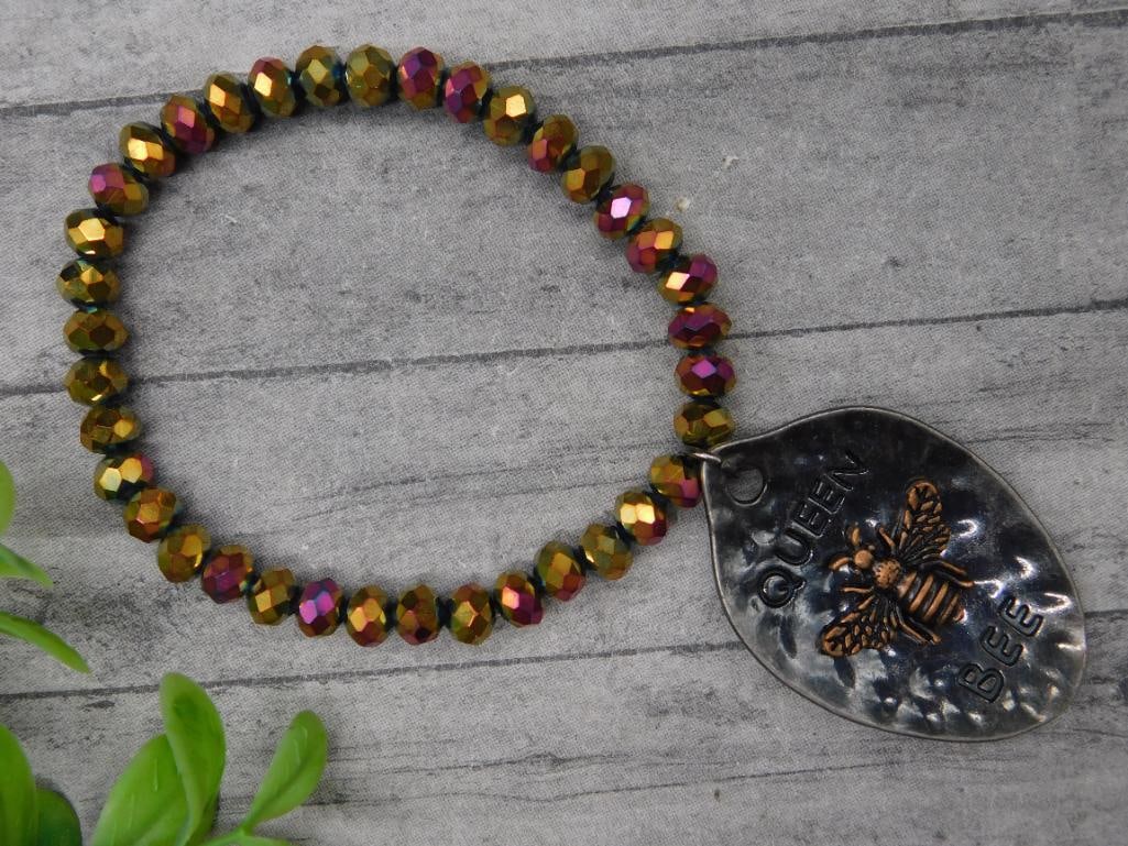 Beaded Bracelet With ?Queen Bee? Metal Charm: A bracelet made of iridescent faceted beads in hues of gold and purple. Features a metal charm with 'Queen Bee' wording and a raised bee design. The charm appears to have a hammered texture, creating