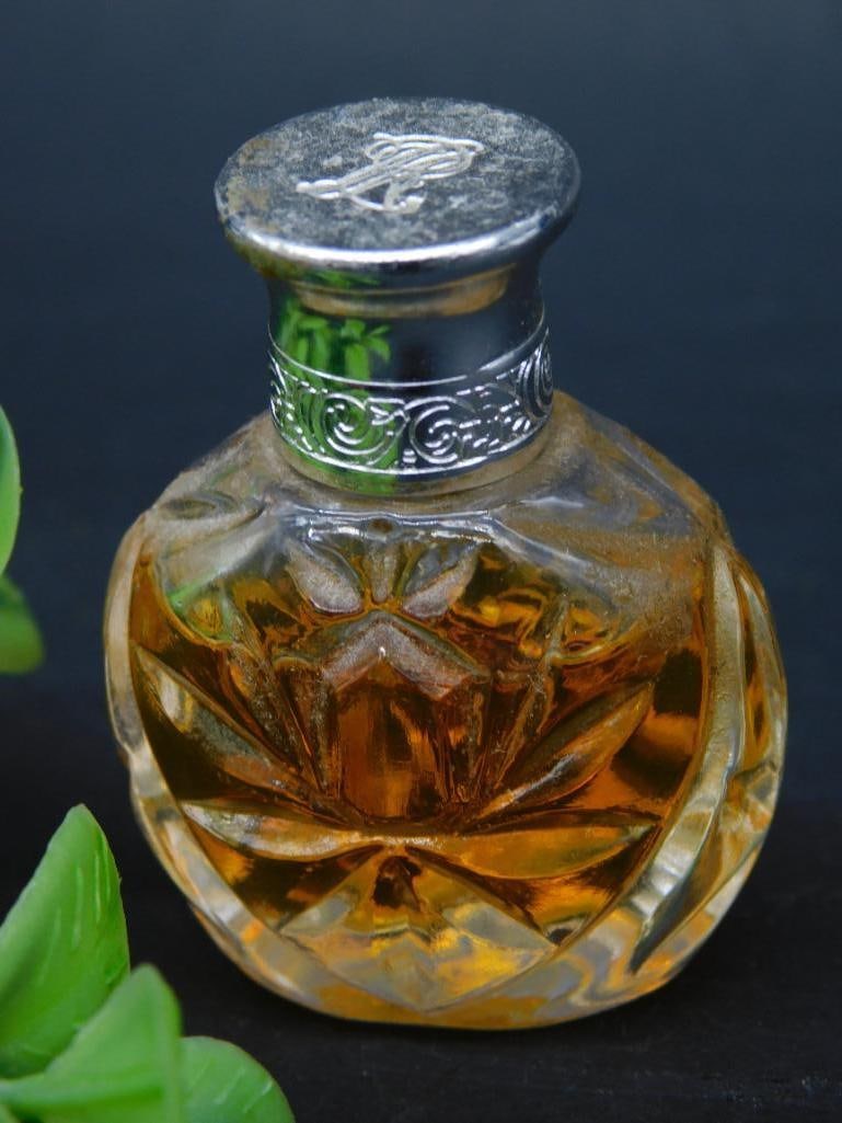Ralph Lauren Miniature Perfume Bottle Collectible: This is a miniature perfume bottle designed by Ralph Lauren. The glass bottle features an embossed design and holds an amber-colored liquid. The cap is metal with an engraved design. The base of the b