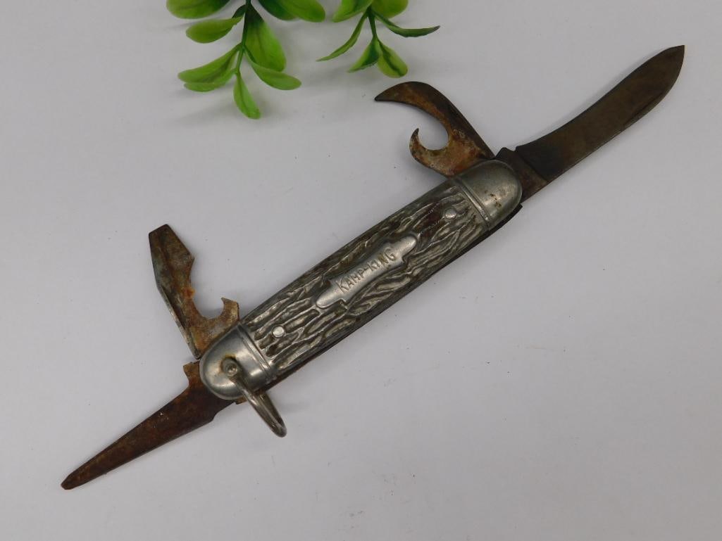 Kamp-King Multi-Tool Pocket Knife with Four Blades: A Kamp-King multi-tool pocket knife featuring four blades/tools: a knife blade, a can opener, a bottle opener, and an awl. The handle displays a textured design with "Kamp-King" engraved. The tools sh