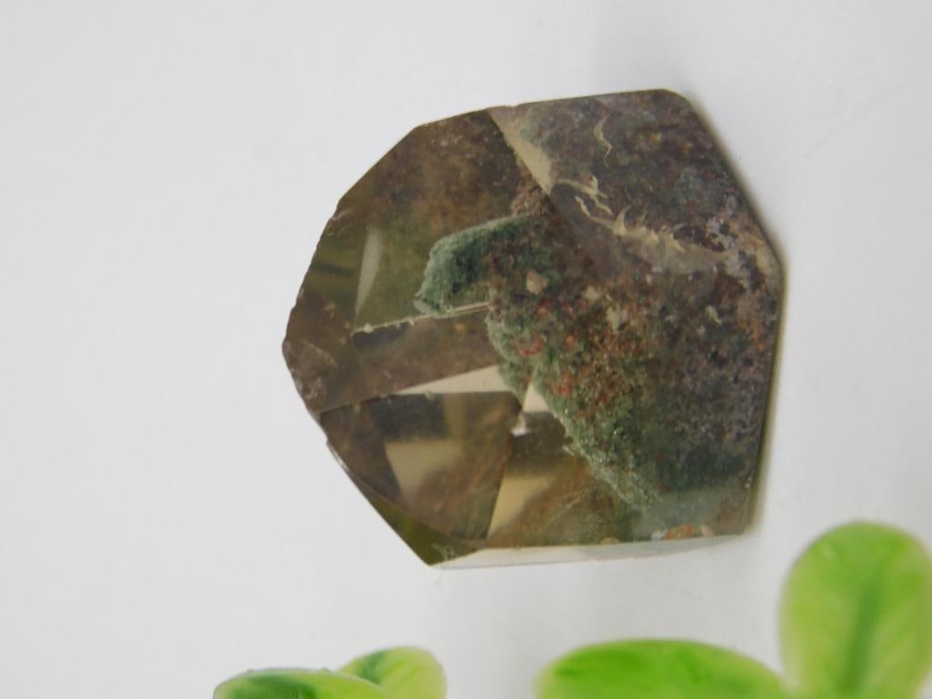 Polished Moss Inclusion Quartz Gemstone, 10 Grams: Polished quartz gemstone featuring natural moss-like inclusions. Weighs 10 grams as indicated. Hexagonal cut with visible internal textures. Suitable for gem collectors or jewelry making. Shown next t