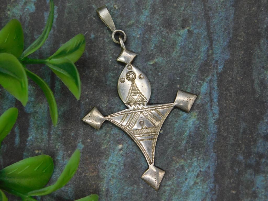 Sterling Silver Geometric Pendant with Tribal Design: Sterling silver pendant featuring a geometric shape with tribal-inspired etchings. The front side is intricately detailed with a symmetrical pattern, while the back is plain with minor surface wear. T