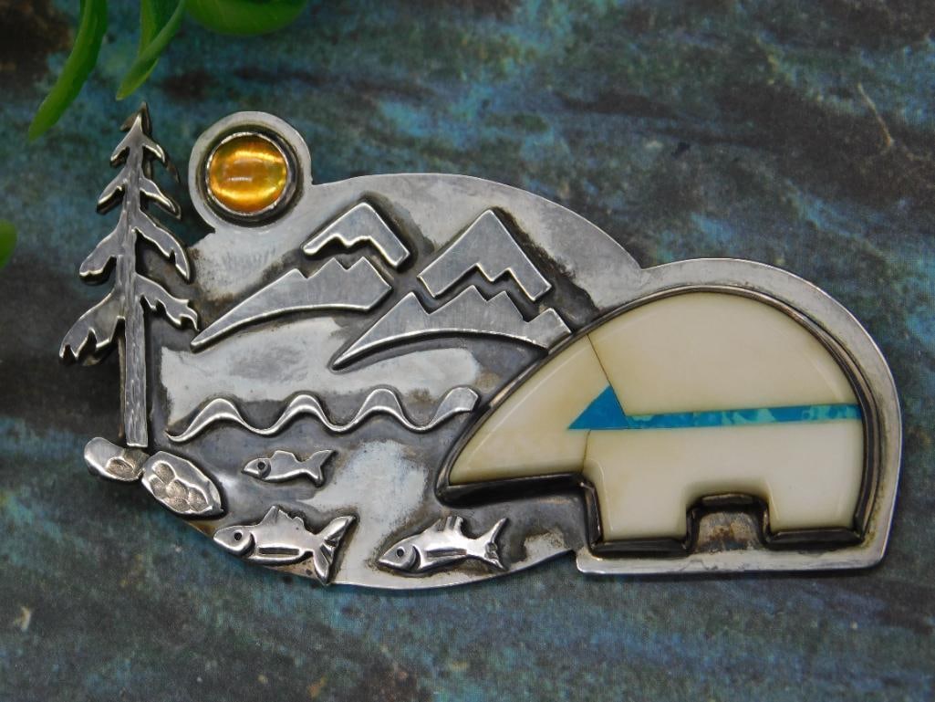 Sterling Silver Wildlife Scene Brooch with Inlay Design: Sterling silver brooch depicting a wildlife scene featuring mountains, a bear with inlay detailing, a tree, fish, and a sun. Marked '925' on the back, indicating sterling silver composition. Includes 