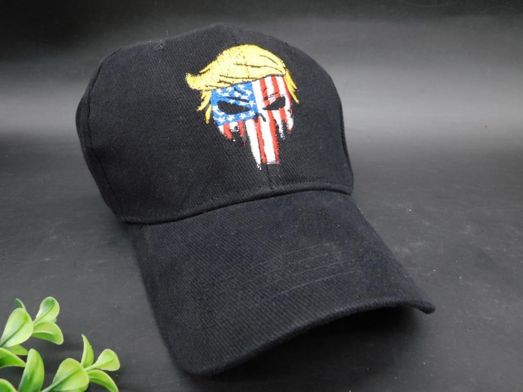 Black Baseball Cap with Embroidered American Flag Design: Black baseball cap featuring an embroidered design on the front. The design includes an image of a skull with the American flag motif and yellow hair. Adjustable back strap for sizing. Utilitarian and