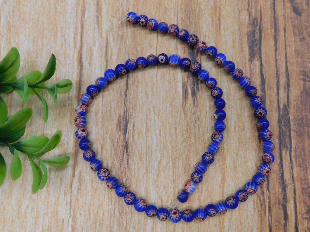 AFRICAN TRADE BEADS ROCK STONE LAPIDARY SPECIMEN: A single strand of blue and red patterned glass beads. The beads are uniformly sized and showcase decorative patterns in red and white against a blue background. Exact dimensions and bead count unspec
