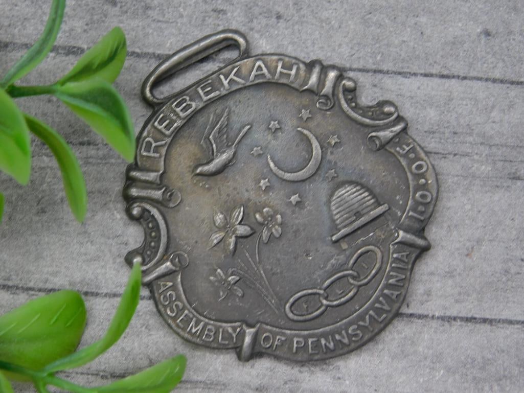 ODD FELLOWS WATCH FOB VINTAGE ANTIQUE: Metal pendant with ?Rebekah? text and various symbols; marked ?Assembly Of Pennsylvania I.O.O.F.?; includes bird, flower, moon, stars, and chain links.