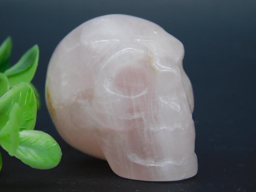 Carved Rose Quartz Skull Sculpture: Hand-carved rose quartz skull crafted from translucent pink stone. Compact size, as shown next to a ruler. Multi-angle view displays natural inclusions inherent to rose quartz.
