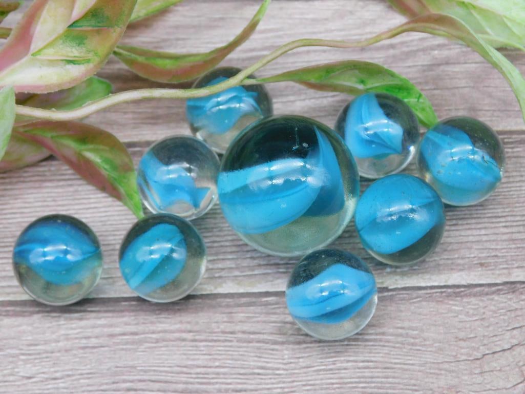 Set of 8 Clear Marbles With Blue Swirl Accents: This collection includes 8 clear glass marbles, each featuring vibrant blue swirl accents within. The set varies in size, as indicated by the ruler shown in the image, with all marbles clean and free 