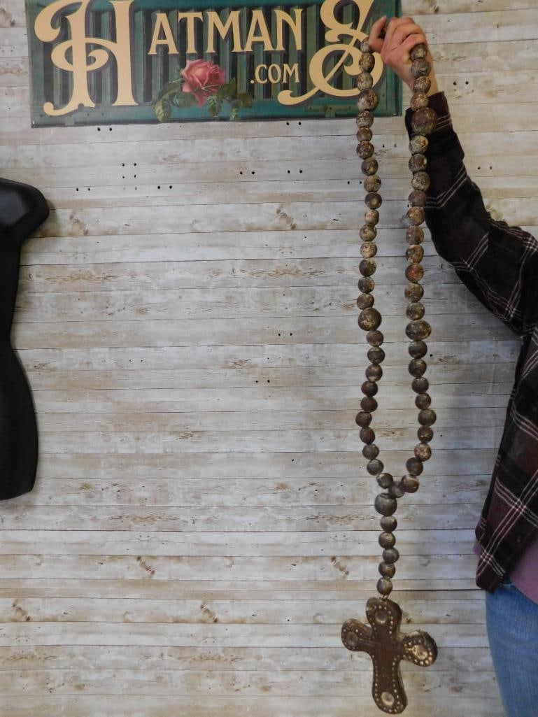 Large Decorative Beaded Metal Cross With Chain: Large decorative metal cross attached to a long strand of beads. The cross features an embossed design with circular patterns. The beads have a weathered appearance, possibly made of metal or another