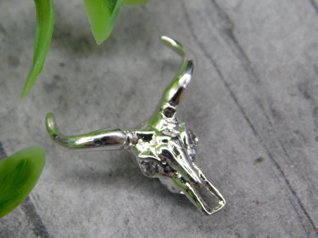 Silver Bull Skull Charm with Longhorn Design: Silver bull skull charm featuring a longhorn design. Compact size ideal for jewelry use. Detailed craftsmanship, and shown next to a coin for scale.