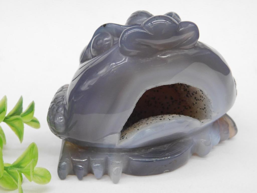 Carved Agate Frog Sculpture with Textured Detail Rock Stone Lapidary Specimen: Carved agate sculpture featuring a frog design with textured detailing throughout. Made of polished gray agate, showcasing color variations and natural patterns. The base showcases a hollowed mouth de