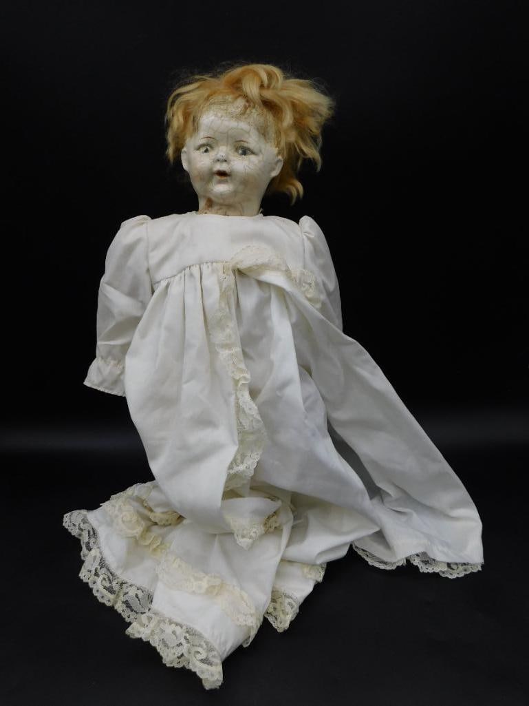 Porcelain Doll With White Lace Dress and Blonde Hair: Porcelain doll featuring a white lace dress with intricate details and blonde hair styled in a loose arrangement. The doll shows natural crackle finish on its face, indicative of aging. Includes a rul